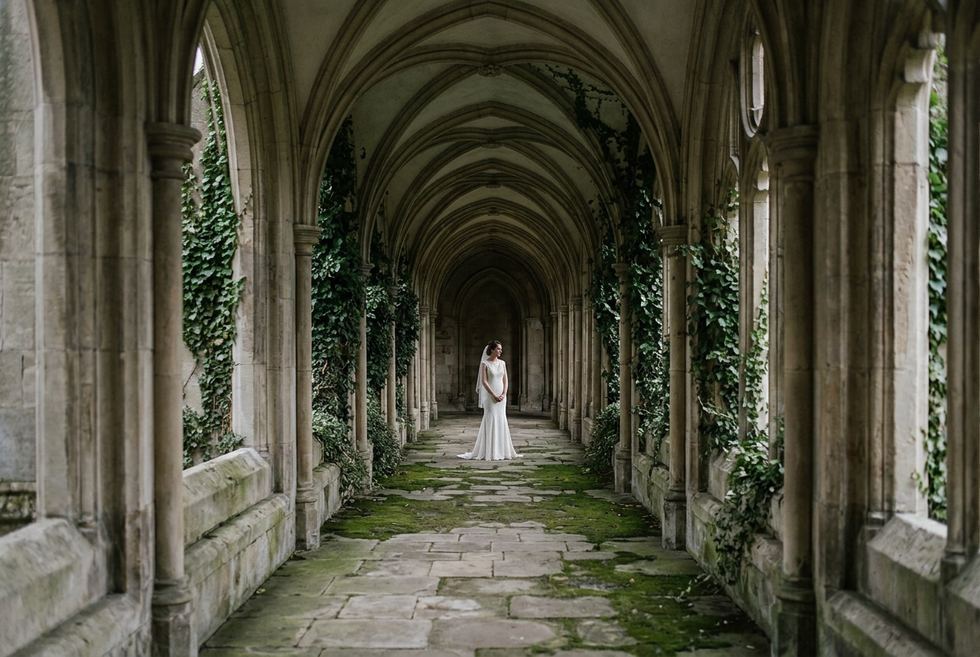 Mariée vue de loin sous une galerie de cloître, à travers les arcades
