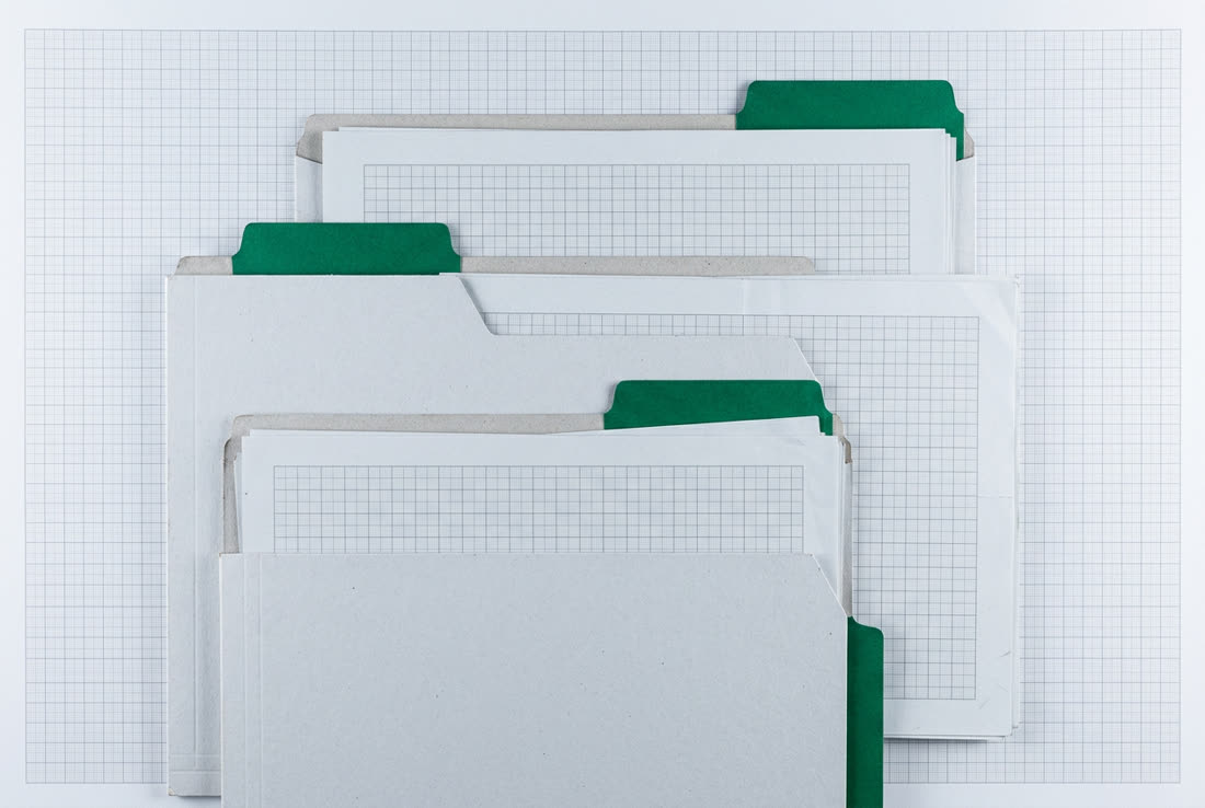 Trois dossiers cartonnés à onglets verts, décalés, des feuilles quadrillées qui dépassent.